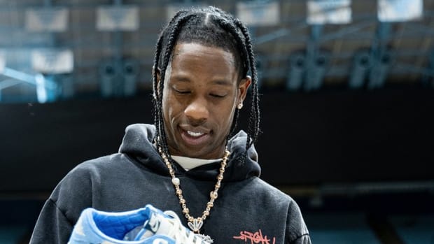 Travis Scott holds blue and white Air Jordan sneakers at a North Carolina Tar Heels basketball practice.